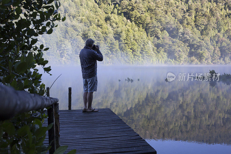 日出时分，一个成熟的男人在湖边的码头上拍照，