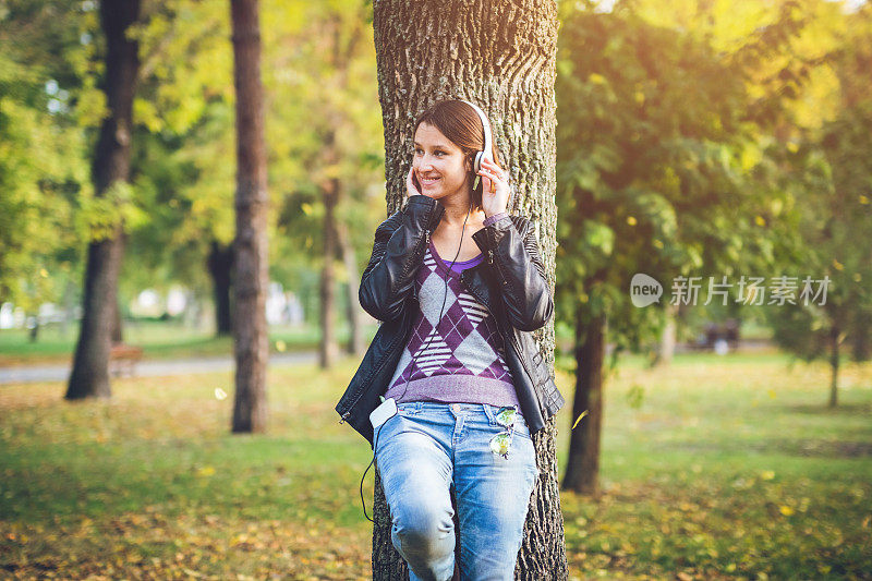 女人戴着耳机站在树旁听音乐。