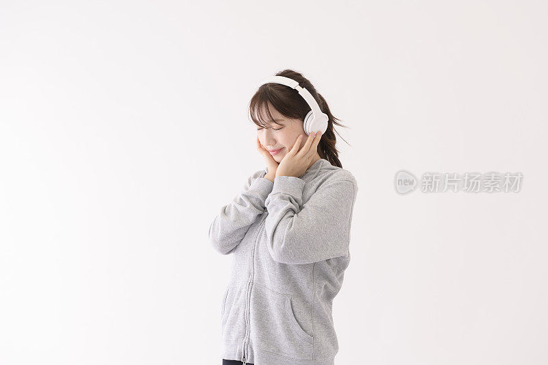 一名年轻女子在白色背景前戴着耳机欣赏音乐。