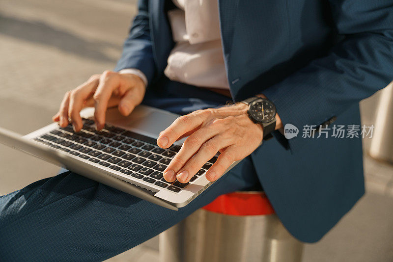 一张侧视图，一个商人的手躺在膝盖上，在他的笔记本电脑上打字