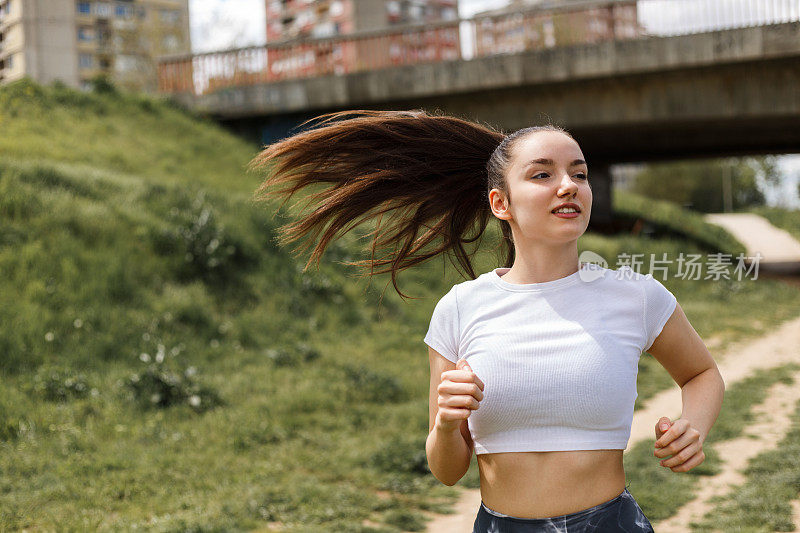 女孩在中午的阳光下在河边跑步。