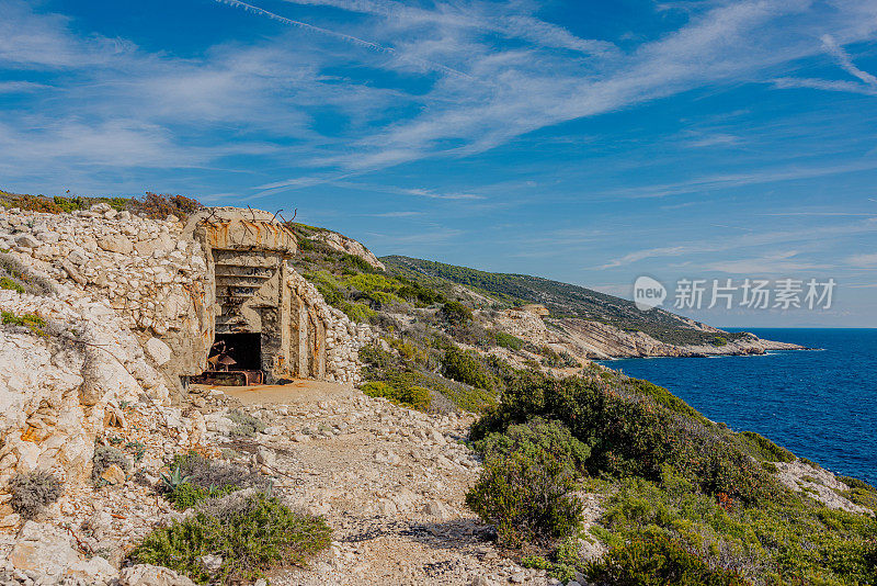 岛上一座山的山顶上有一个二战时期的旧地堡，地堡里有一个陈旧的棕色生锈的炮筒，背景是大海