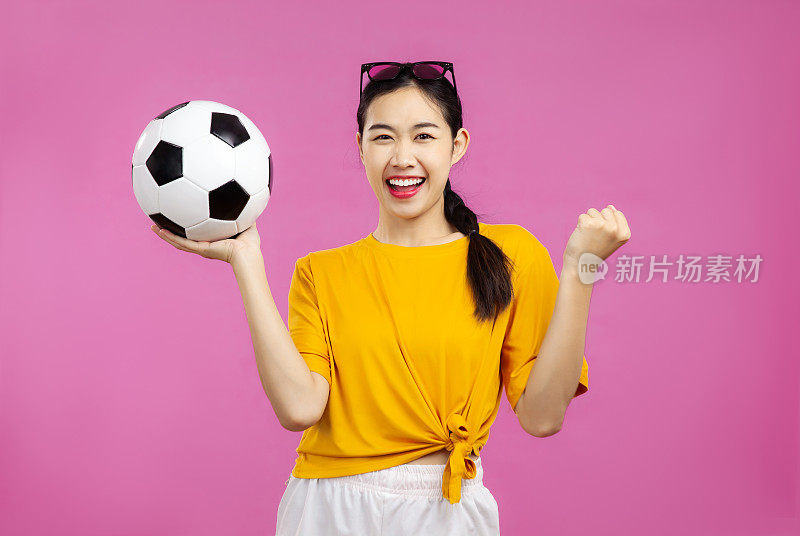 开朗的亚洲年轻女子在孤立的粉红色背景下拿着一个足球，足球和人，国际足联世界杯的概念