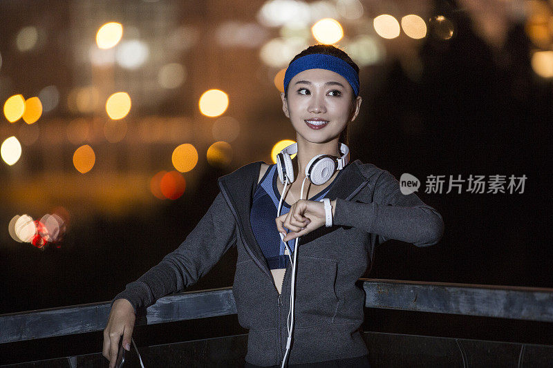年轻的东亚妇女使用手机，同时在夜间的城市街道上进行身体训练-库存照片