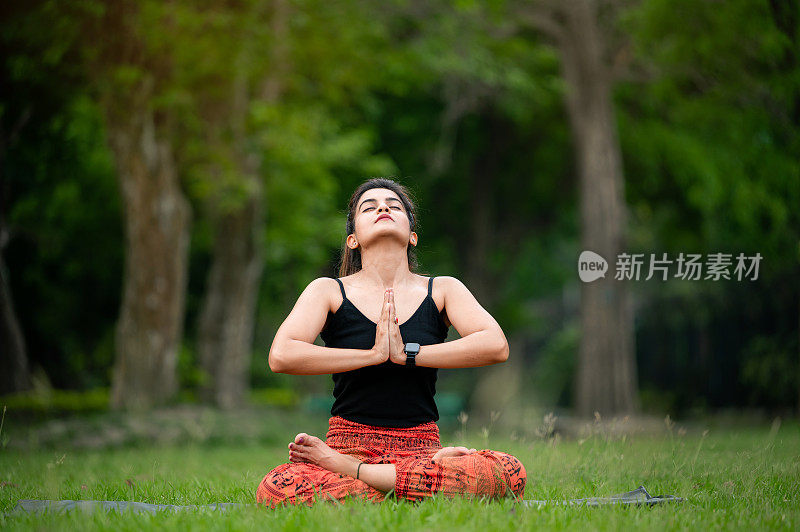 坐在莲花位的女人在户外做合十礼的姿势冥想