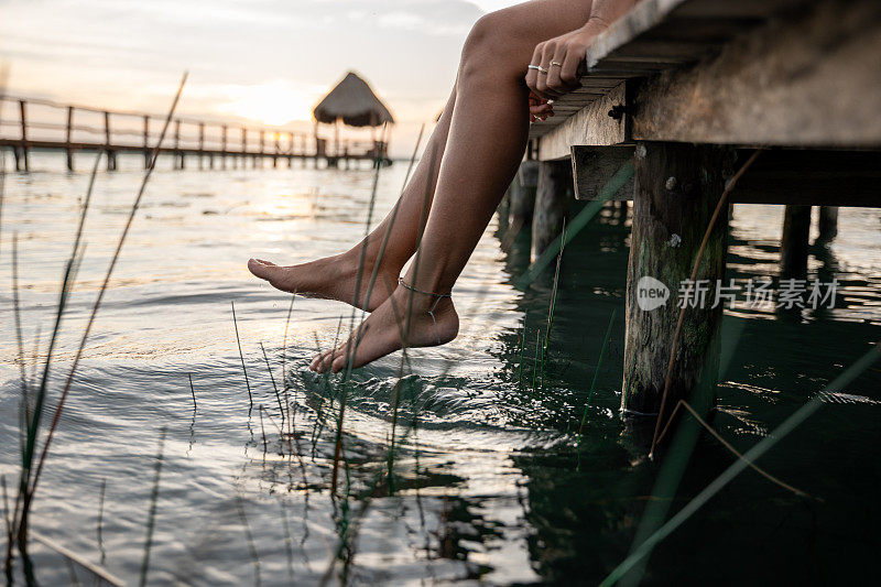 日出时，女人坐在湖面上的码头上，双脚晃来晃去