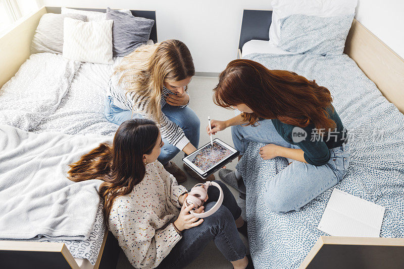 头顶上，三位年轻女性坐在宿舍的床上，一边看平板电脑，一边听音乐