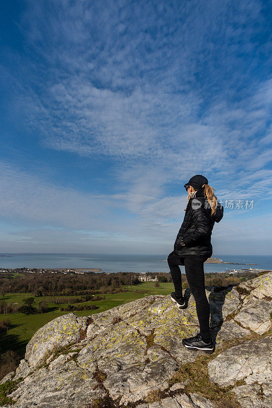 一名女子站在山顶上欣赏爱尔兰霍斯都柏林湾的景色