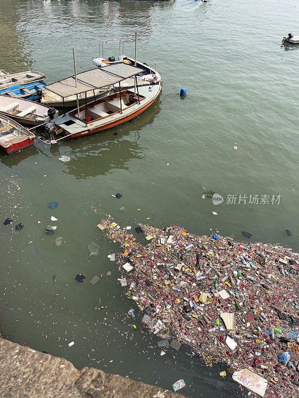 垃圾漂浮在印度之门海滨被污染的海面上，旁边是小木船，水污染，垃圾，垃圾和废物窒息流动的水，高架视图