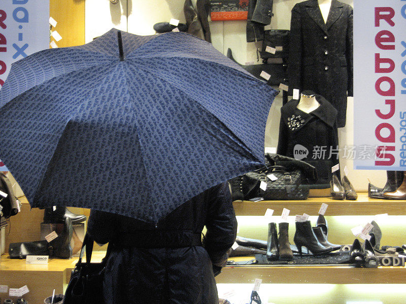 伞下的女人在看时装店的零售展示