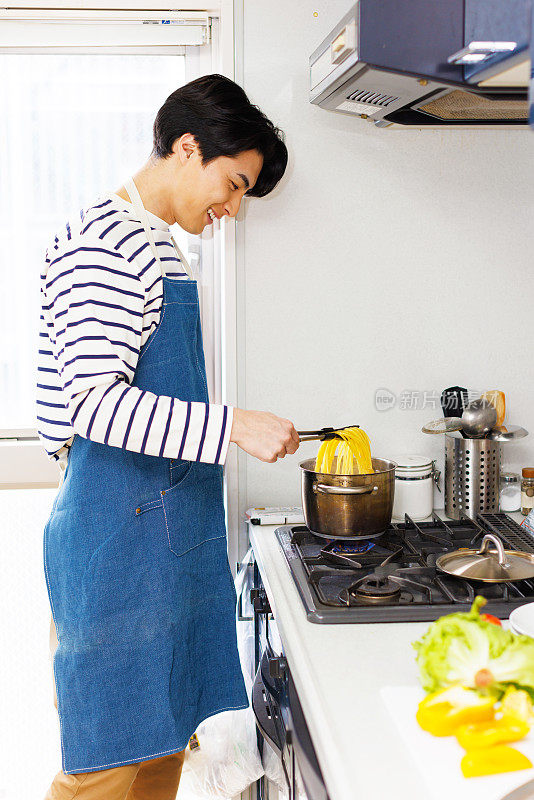 穿着围裙的日本人在厨房里煮意大利面