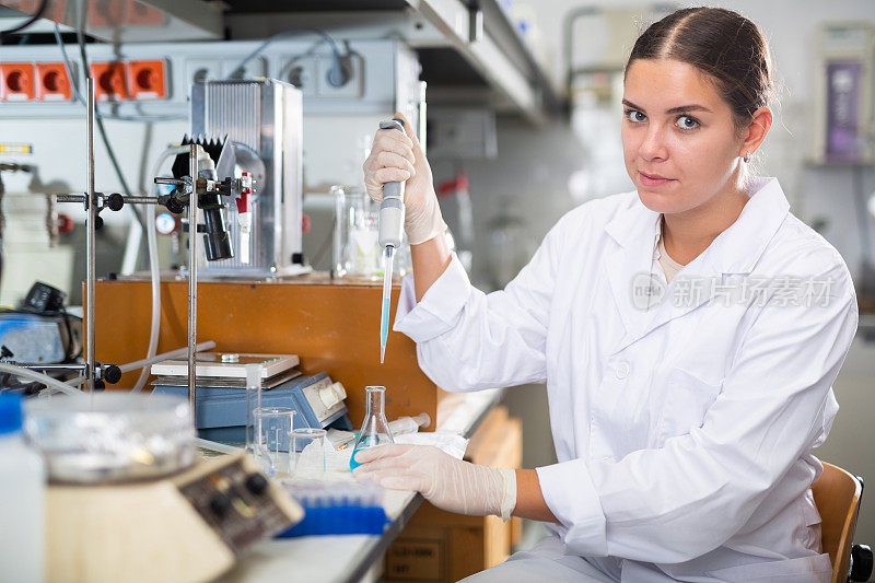 穿着白大褂的聪明的年轻生物学家在现代实验室中使用机械实验室移液器混合化学物质