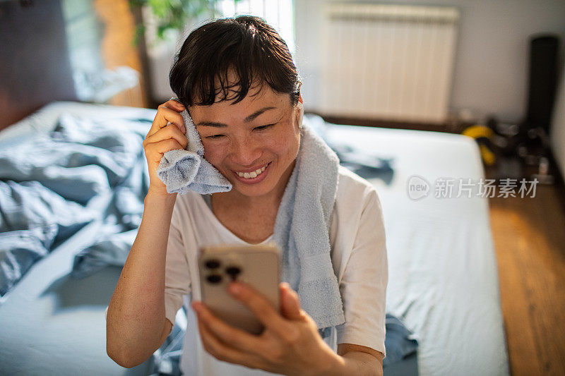 年轻的日本女子在家里锻炼完后使用智能手机