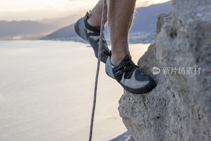 攀岩者的腿攀登海面上陡峭的悬崖