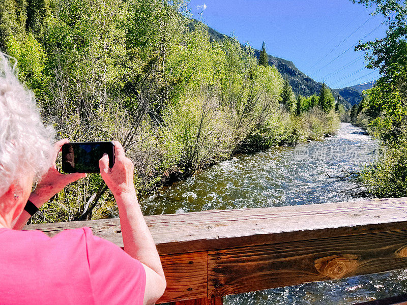 晚春时节，一位老年女游客在科罗拉多州的一条河上拍照