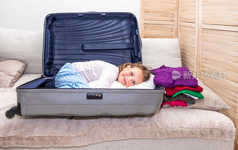 一个白人女孩，7岁，收集东西，一个旅行用的手提箱。孩子爬进一个大手提箱。