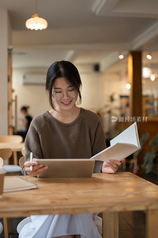 一个美丽的亚洲女人正在使用她的平板电脑，在线学习，并在咖啡店远程工作。