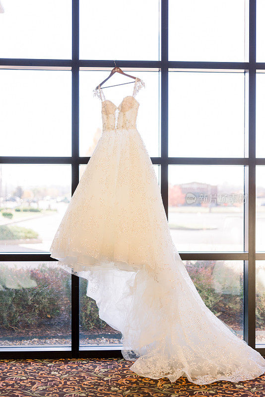 一件漂亮的白色婚纱，长长的裙摆挂在方形的窗户上