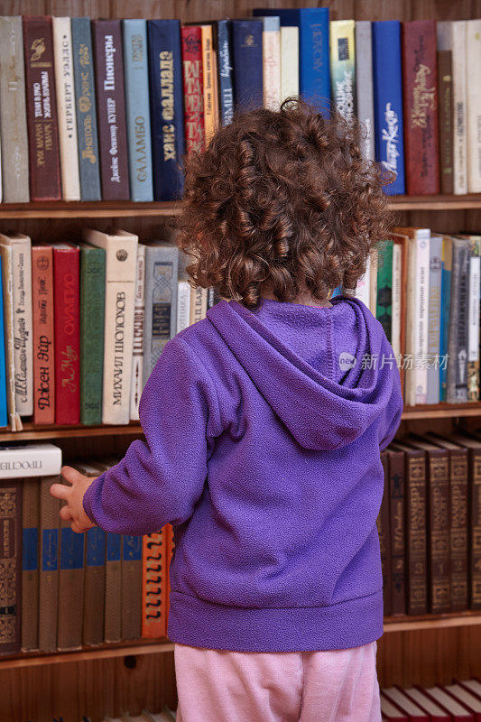 一个小女孩站在书架前的后视图