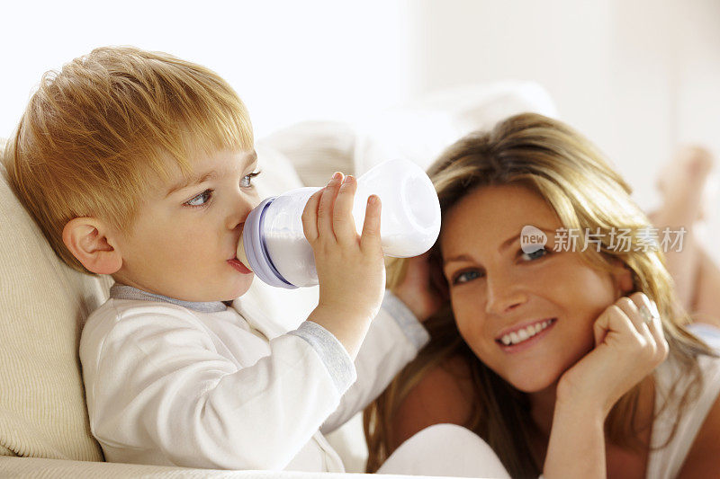 母亲和蹒跚学步的孩子在家喝奶瓶里的牛奶