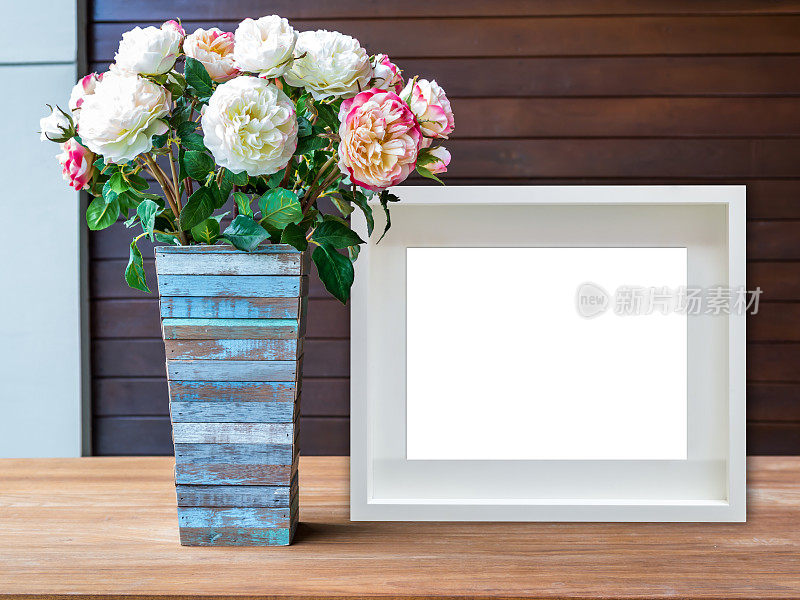 木桌上的空白白色画框和花瓶