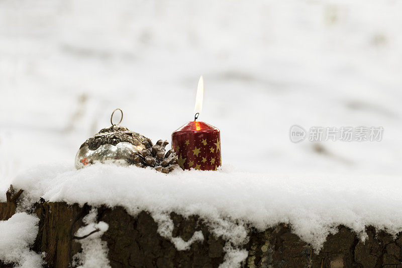 燃烧的蜡烛，圣诞的小装饰品和松果在雪中