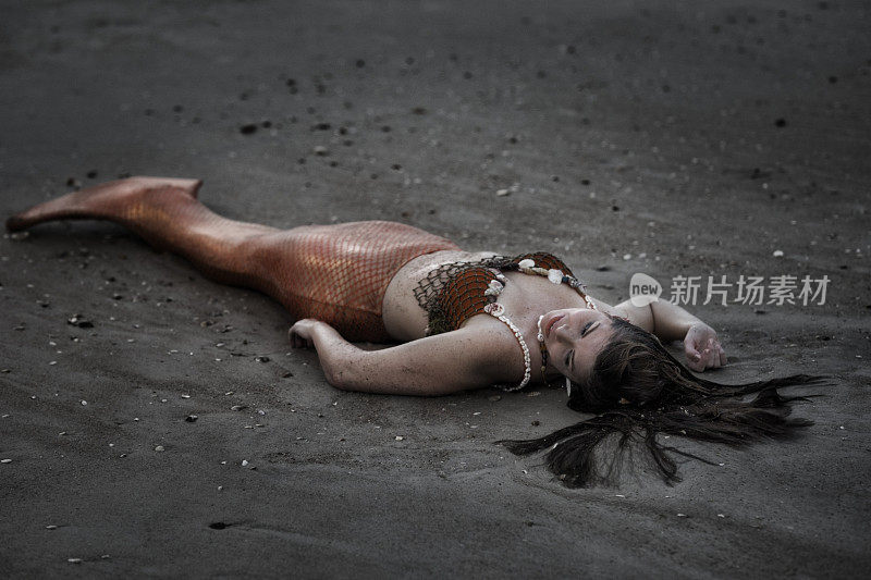 精疲力竭的美人鱼晚上躺在沙滩上