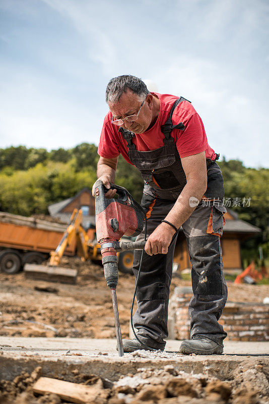 成熟的建筑工人在室外钻孔。