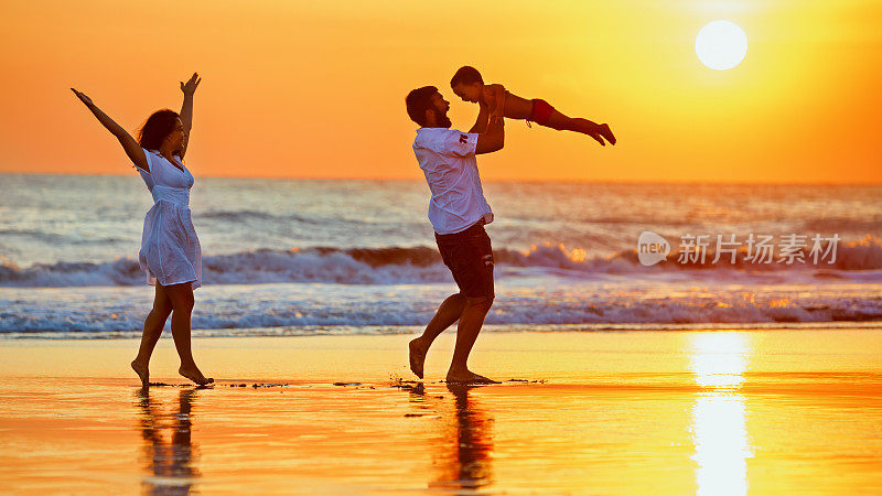 快乐的家庭漫步在日落的海滩上