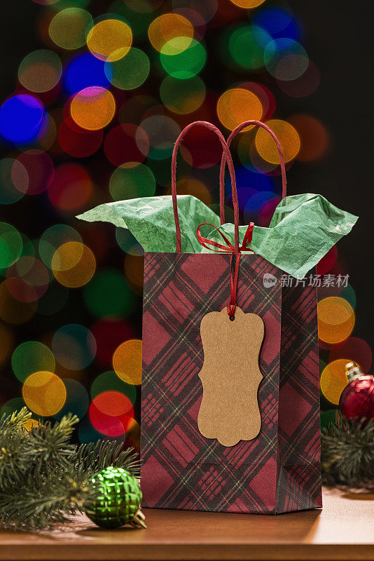 红色格子礼品袋与礼物标签和散焦从圣诞树。