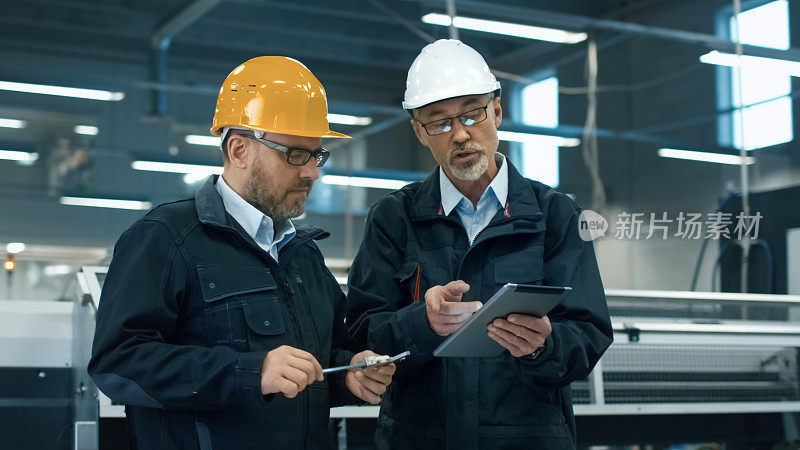 站在工厂里，两位工程师戴着安全帽在平板电脑上讨论信息。