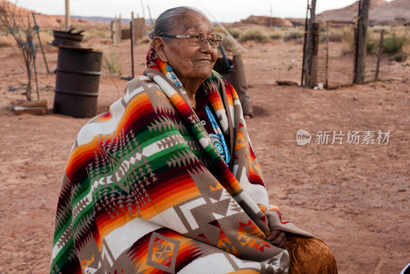 黄昏时分，美丽的纳瓦霍奶奶坐在院子里，披着传统的手工毯子