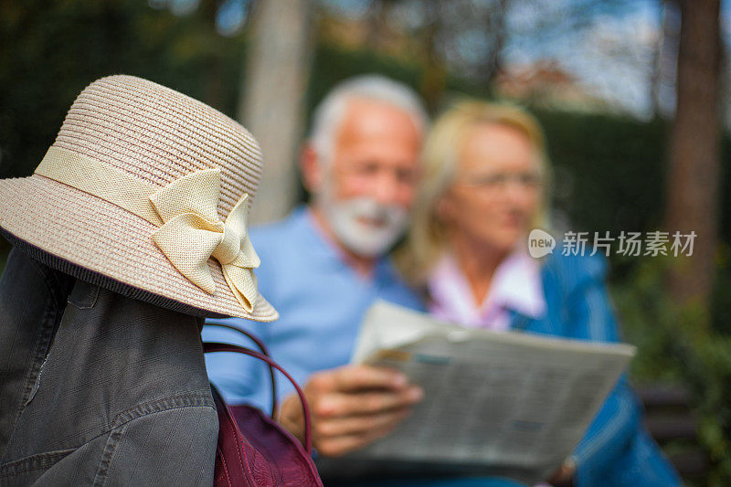 一对老夫妇在公园里读报纸，在旅行中休息