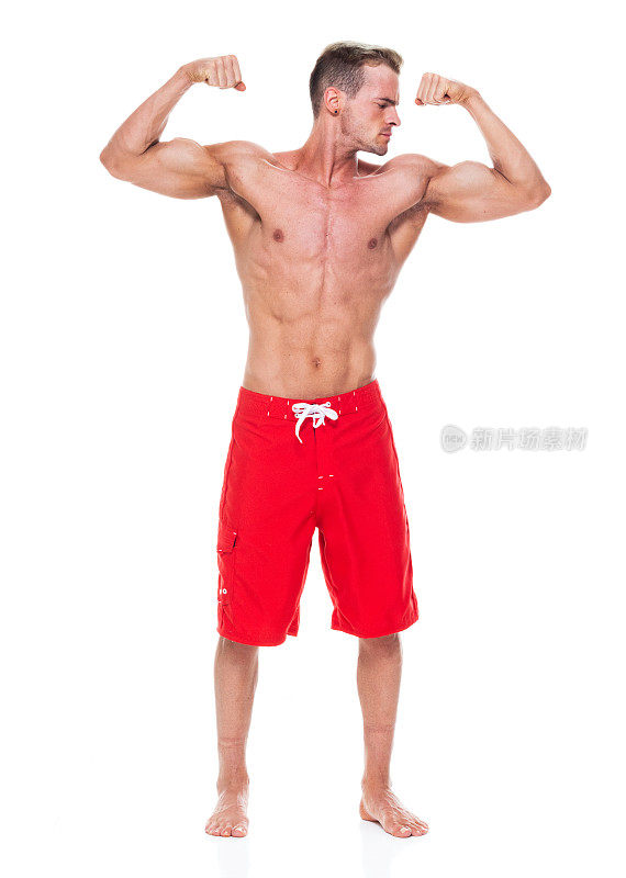 英俊的肌肉男子谁是赤膊和穿着板短裤和弯曲他的肌肉