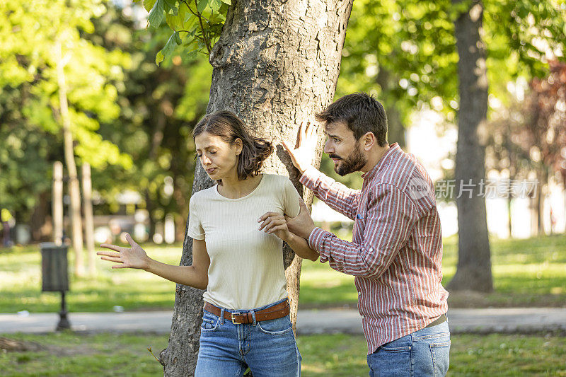 一对年轻夫妇在公园里吵架。年轻夫妇有一个夏天的一天争吵。站在公园外面，困惑的年轻女子打着手势，看着她的男朋友