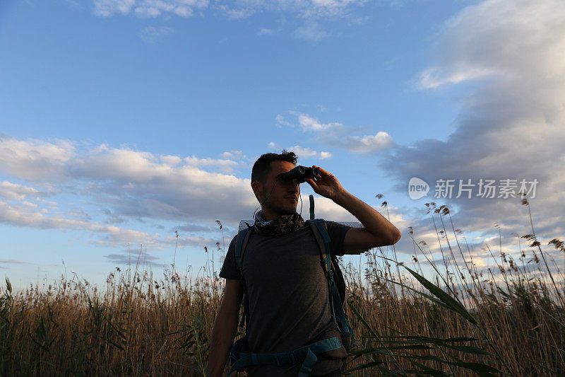 年轻的旅行者用双筒望远镜观察大自然。湖泊、日落和旅人