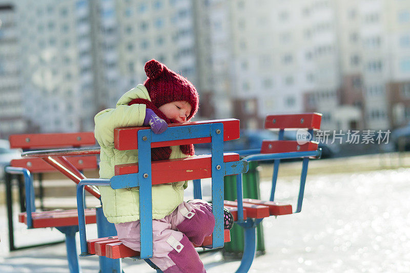 一个2岁的小女孩在室外骑旋转木马，在一个寒冷的阳光明媚的冬日。