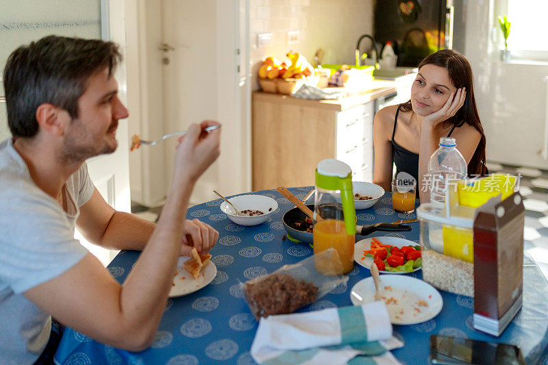 年轻女子深情地看着正在吃早餐的男友