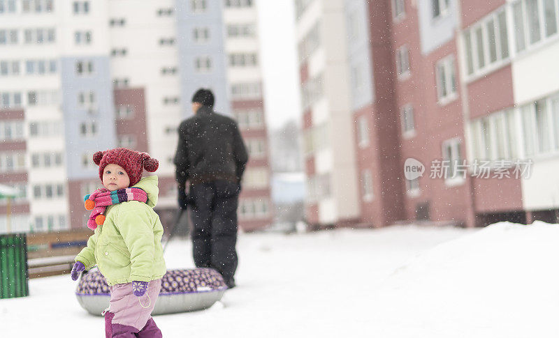 70岁的老人，爷爷和孙女扛着雪筒在雪中行走。