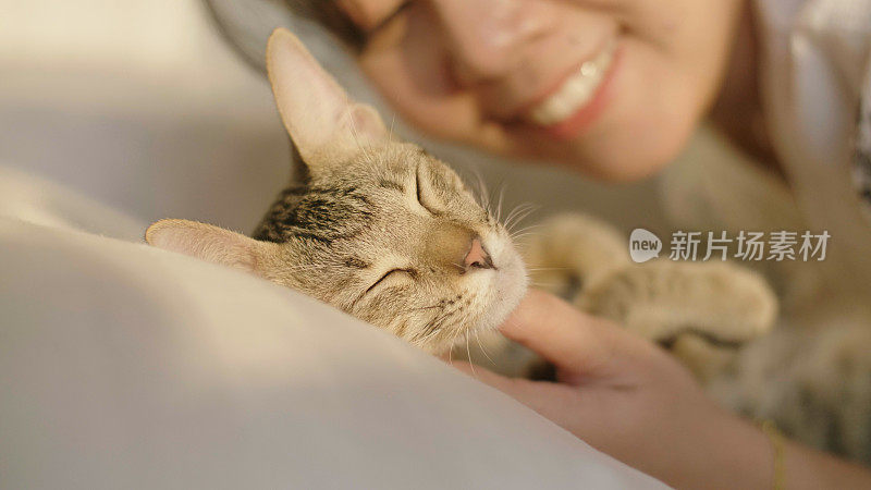 一位年轻女子在卧室白色的床上抚摸她的猫。