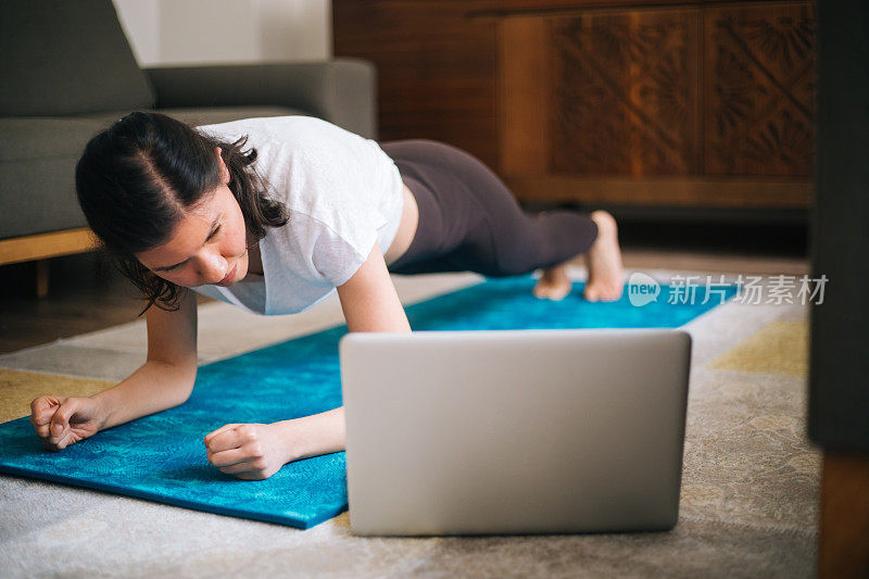 女孩在家训练，做平板支撑，在笔记本电脑上看视频