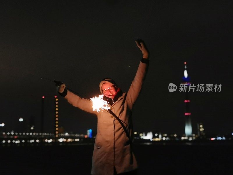 一个寒冷的冬夜，年轻女子在Düsseldorf地平线前用闪亮的烟火庆祝