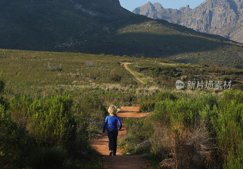 一个小男孩在山里的单行道上跑步