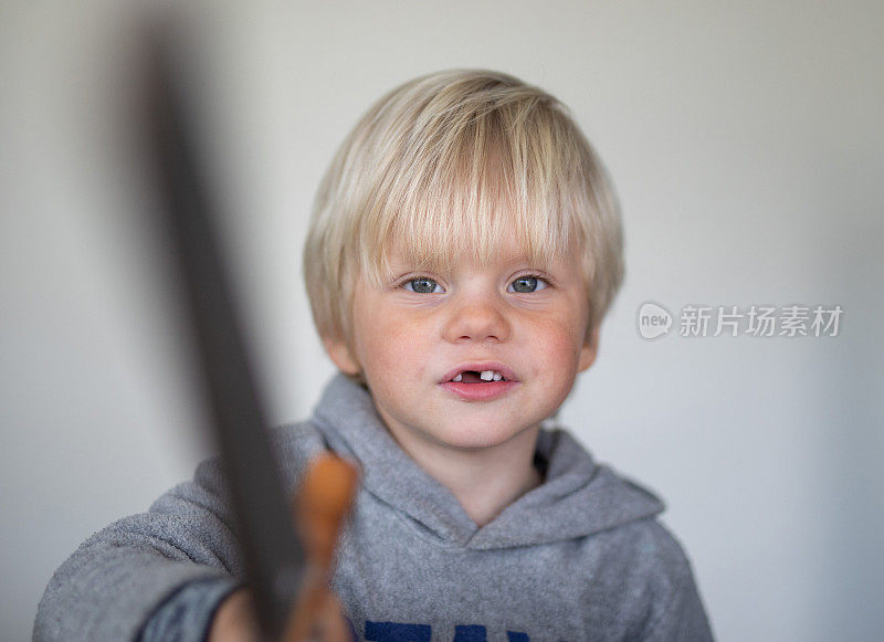 一个小男孩在白色屏幕前摆姿势玩木剑。