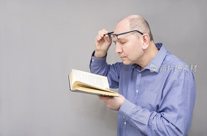 一个视力受损的白人，在读一本书。肖像，戴眼镜的男人，