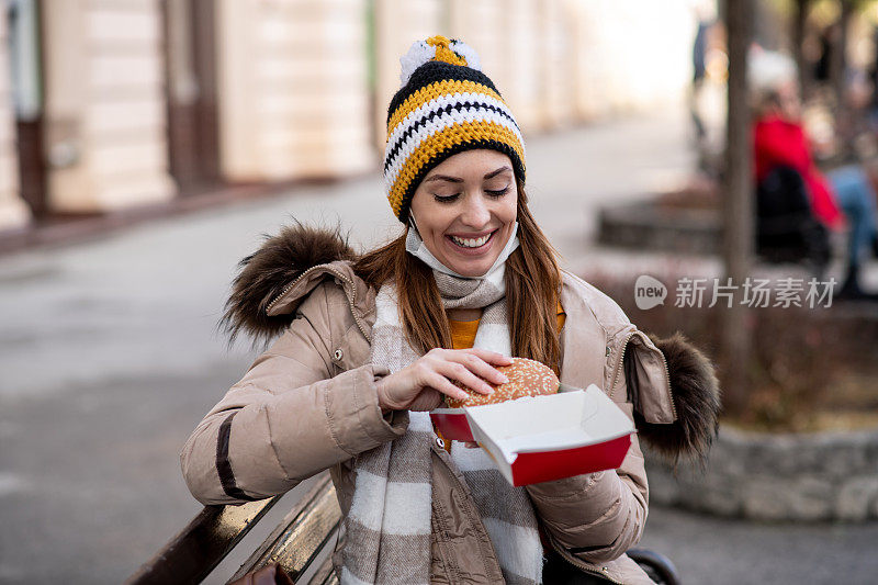 冬季。女孩在外面吃饭，坐在长凳上。