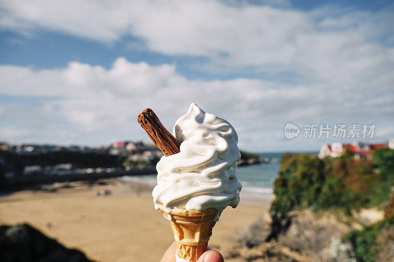 在一个晴朗的秋日，康沃尔纽基的托万海滩上，一只手拿着一个融化的冰淇淋。