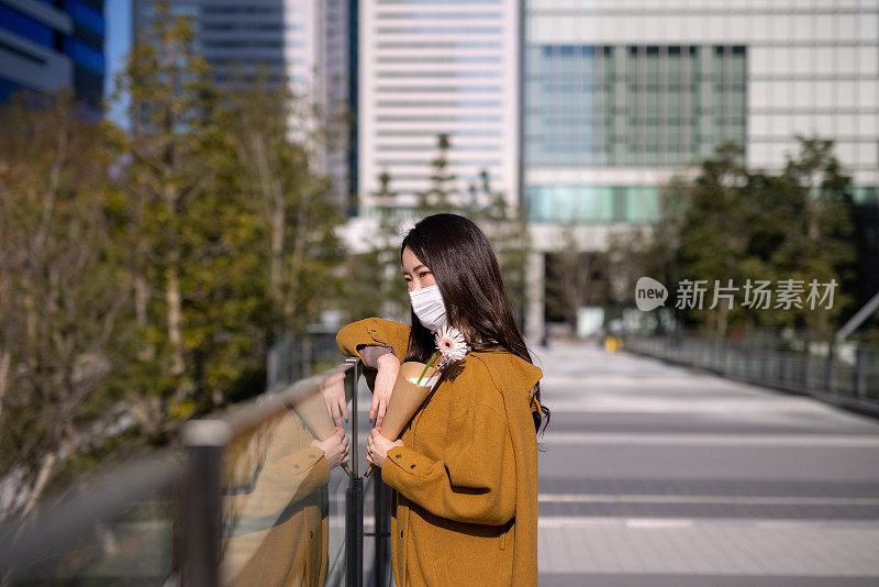 年轻女子戴着保护面罩站在城市里，手里拿着一朵花