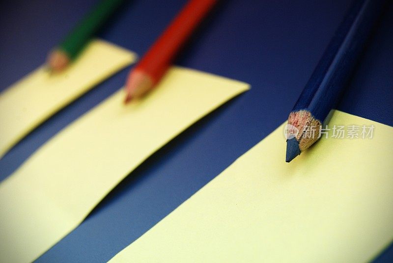 三种原色铅笔，RGB或红、绿、蓝排成一排，贴在黄色的便利贴上，贴在深蓝色的背景上，重点放在蓝色铅笔上