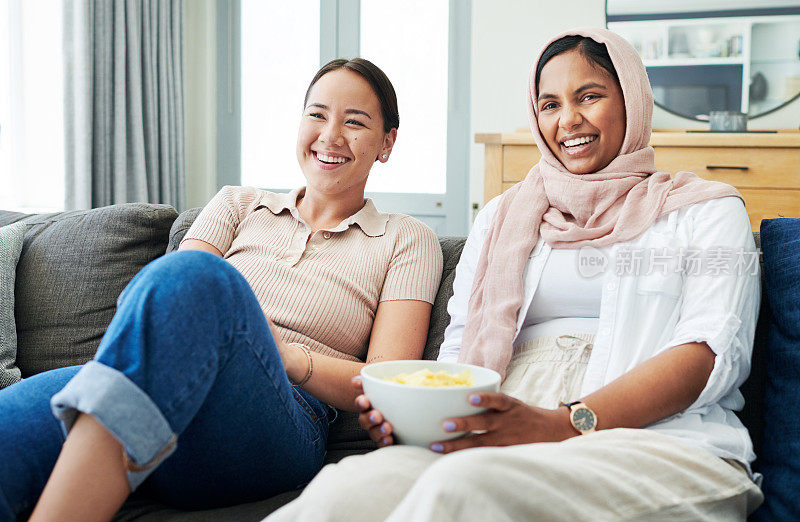 两个女人一起坐在家里的沙发上，一边看电影一边吃零食